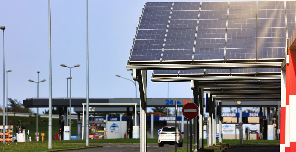 Technicien en tenue de sécurité installant des panneaux solaires sur la structure métallique d'une ombrière de parking industriel